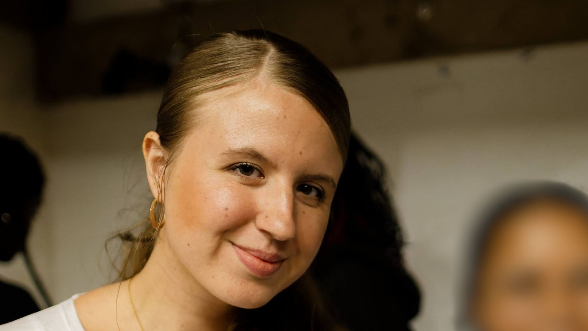 A young lady in a white shirt looking directly at the camera and smiling
