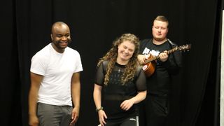 Three people on stage one of them holding a guitar